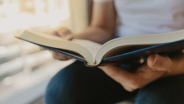 Image of a person reading with a book in their lap. Image cuts off their face