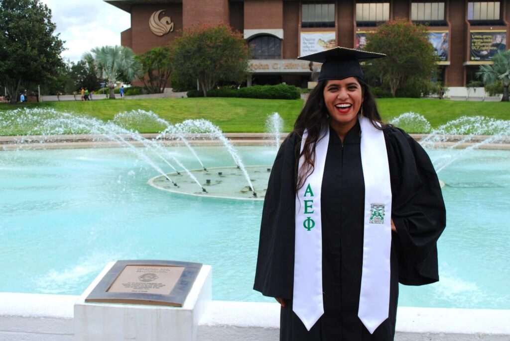 woman in regalia standing in front of UCF fountain