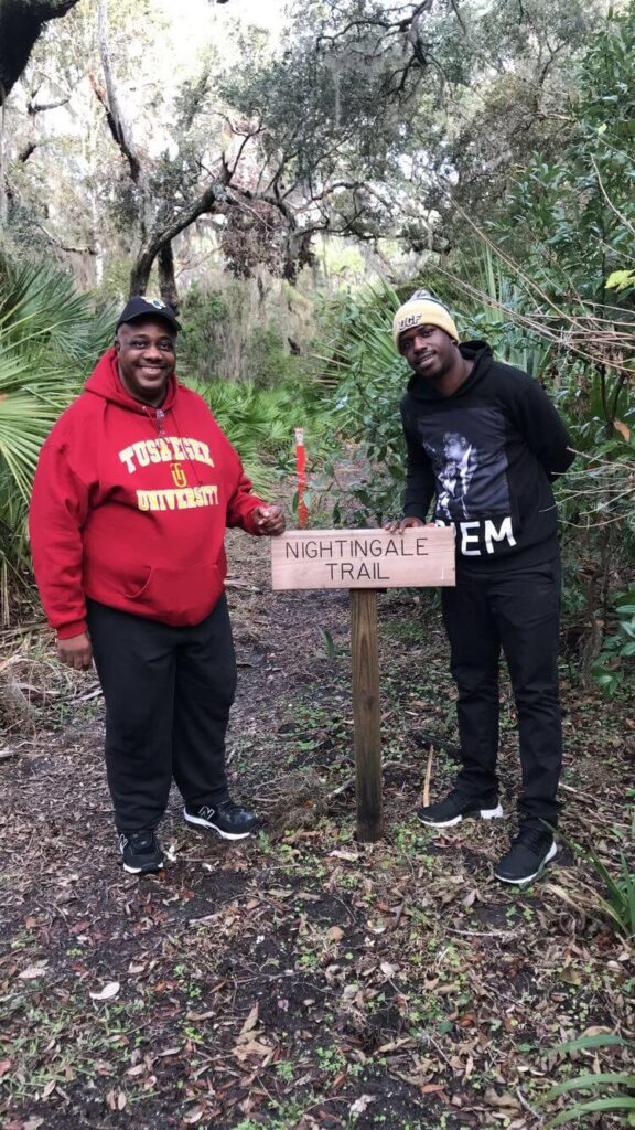 two men standing in front of a sign in a forest