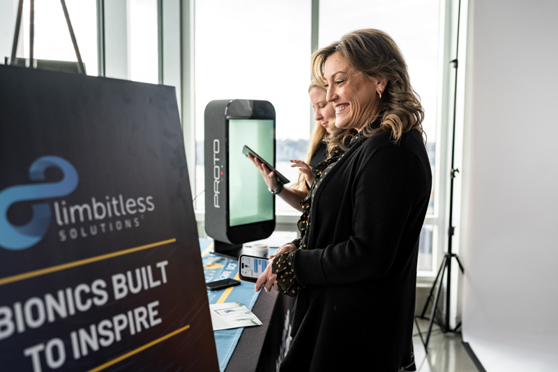 Two women at a tech expo booth for Limbitless Solutions, smiling as they interact with devices on display.