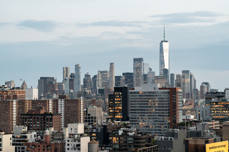 New York City skyline at dusk with One World Trade Center towering above shorter buildings.