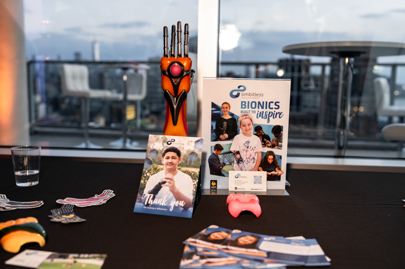 Promotional table with an orange robotic hand, brochures, and thank-you cards at a conference booth.