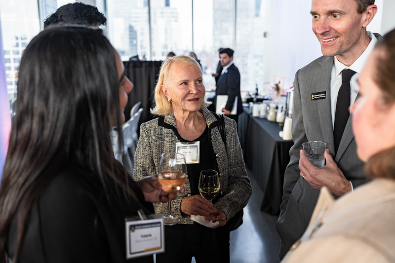Group of professionals at a networking event, chatting and holding wine glasses in a bright office space.