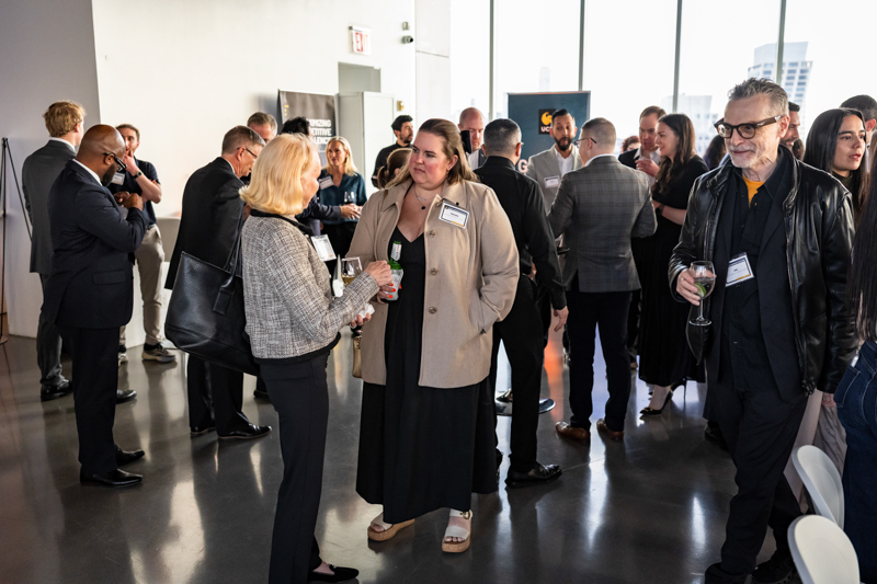 Group of professionals networking at a modern event space, holding drinks and engaging in conversations.
