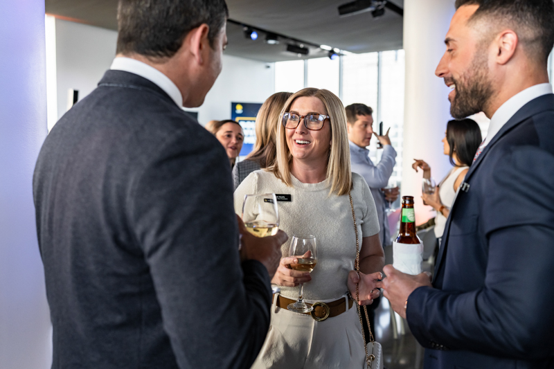 Group of professionals mingling at a modern indoor networking event, holding wine and beer glasses while chatting.