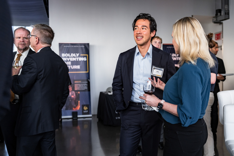 Professionals in a networking event converse; a man in a dark suit chats with a blonde woman holding a glass of wine in a modern venue.