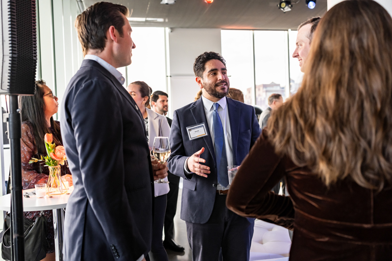 Group of professionals at a networking event, conversing with drinks in hand at a modern venue with flowers on the table.