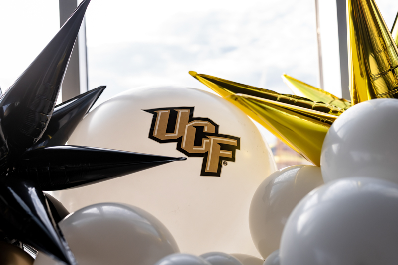 White balloon with the UCF logo, surrounded by black and gold party balloons.