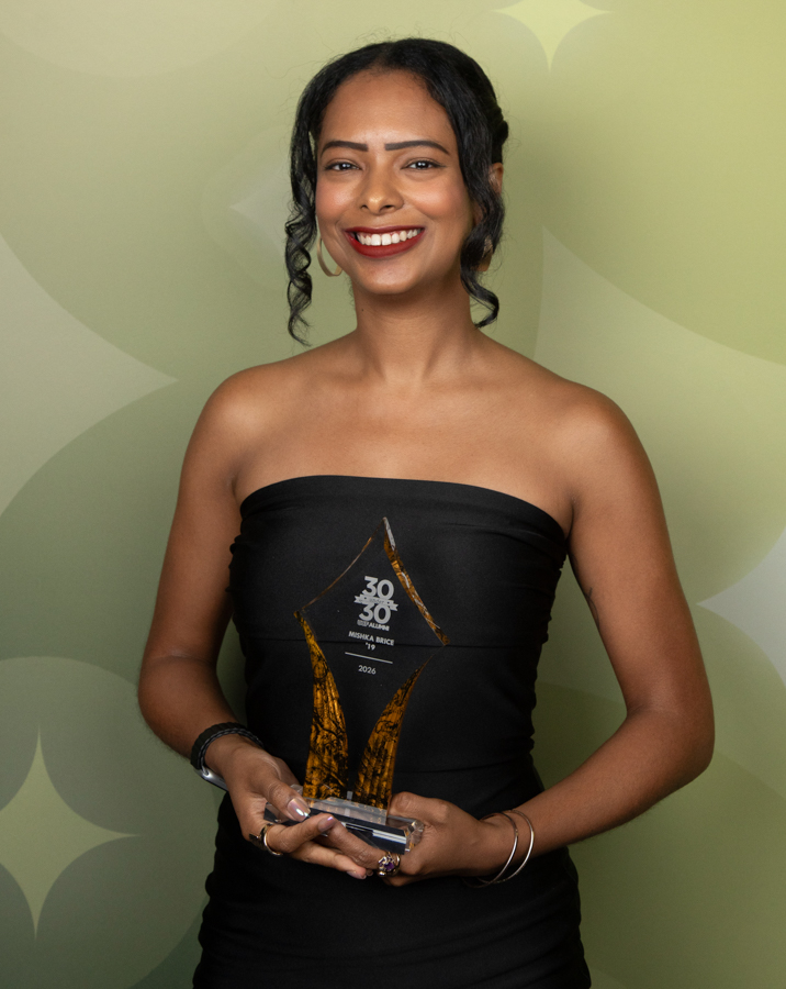 Smiling woman in a black strapless dress holding a glass trophy with both hands.
