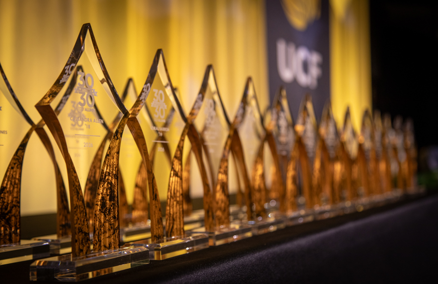 Row of amber glass trophies with 30th-anniversary engravings lined up on a black table at an awards ceremony.