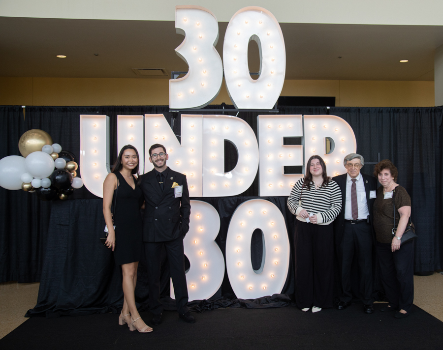 Five people posing in front of oversized, illuminated '30 UNDER 30' letters at an awards event.