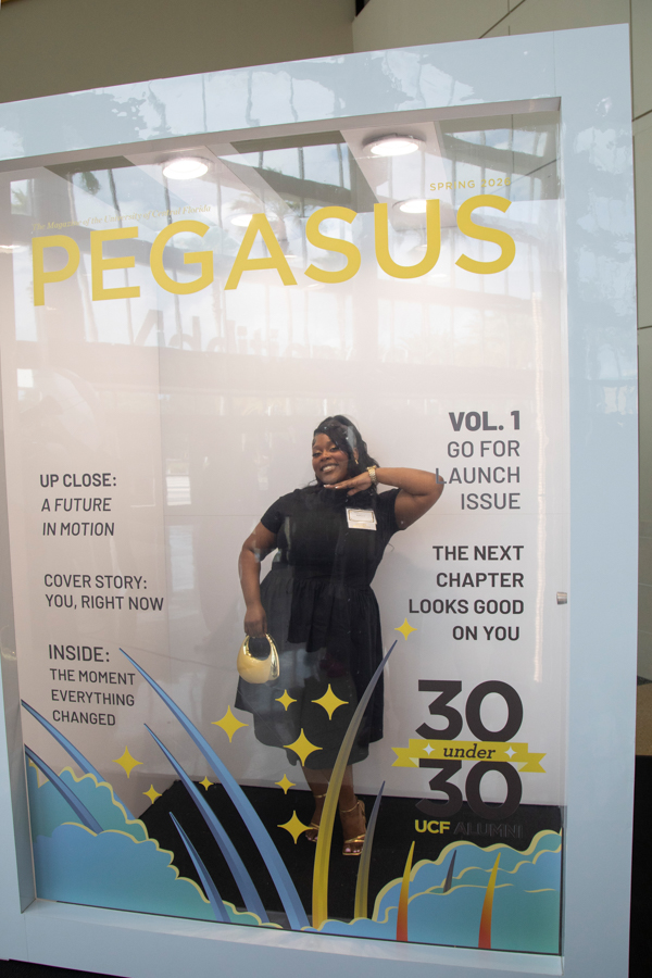 Poster-style magazine cover reading PEGASUS with a smiling woman in a black dress posing in a glass display window; bright yellow title and decorative blue/yellow waves at the bottom, 30 under 30 theme present.