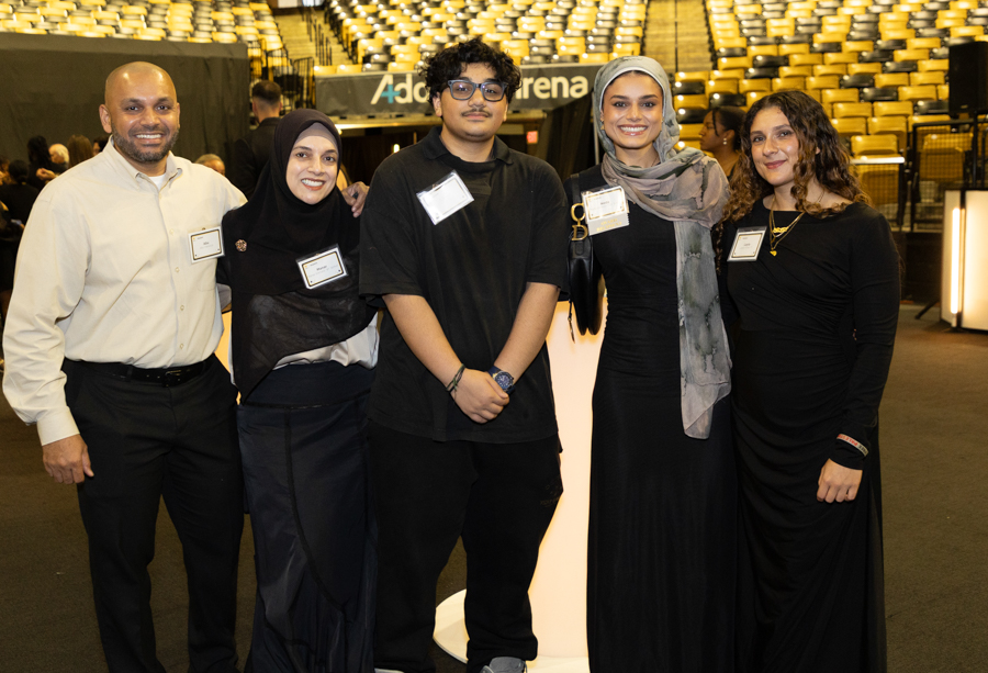 Group of five people posing together at an event in a large auditorium, smiling for the camera.