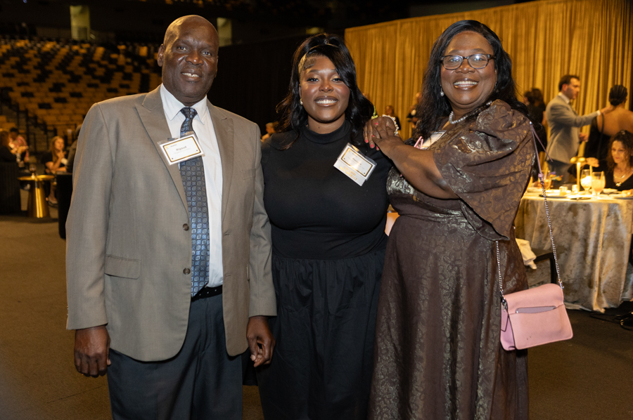 Three adults in formal attire pose for a photo at a banquet, with name badges visible on their jackets.