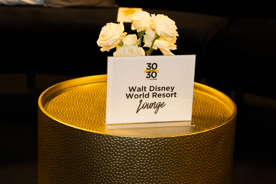 Sign on a gold textured table that reads 'Walt Disney World Resort Lounge' with white roses in the background.