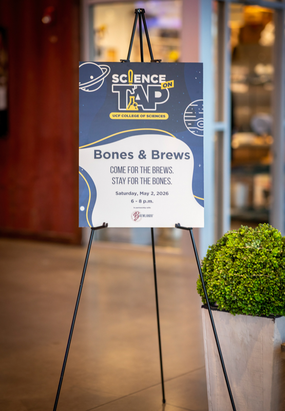 Poster on a tripod advertising 'Bones & Brews' science event at UCF College of Sciences, May 2, 2026, 6–8 p.m.