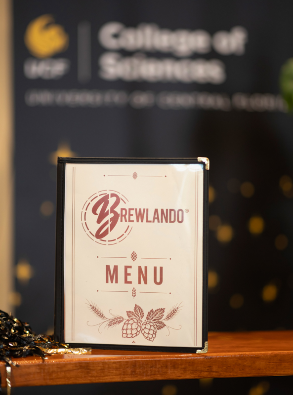 Menu card on a wooden counter featuring the Brewlando logo and the word MENU, with hop and barley graphics.