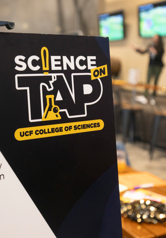Poster reading 'Science Tap' with yellow lab icons at a science event; UCF College of Sciences.