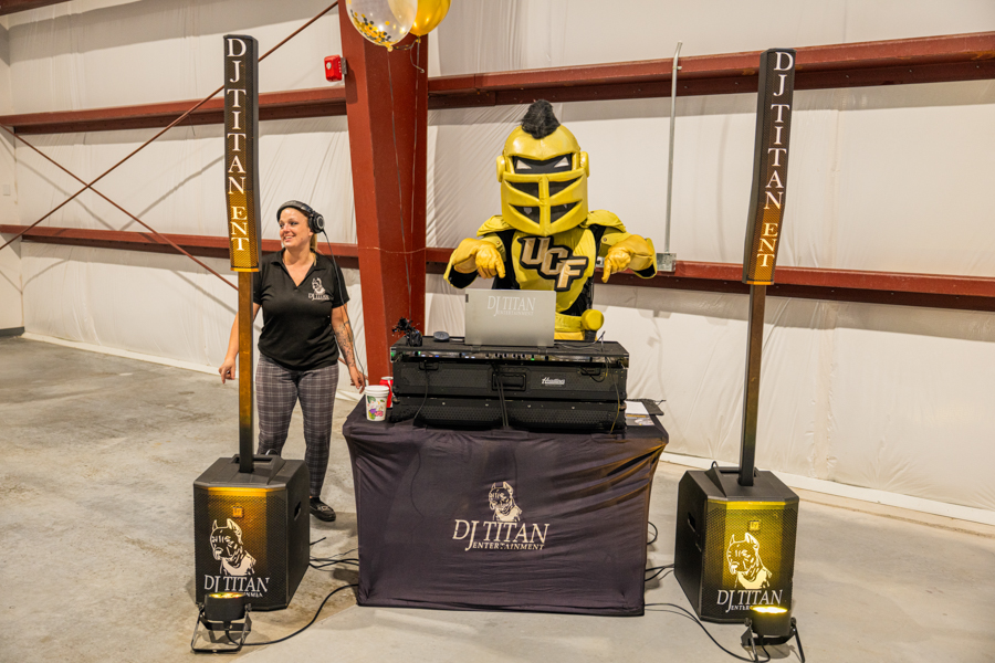 DJ Titan setup with a yellow knight mascot at the mixer, flanked by banners; a woman with headphones stands on the left.