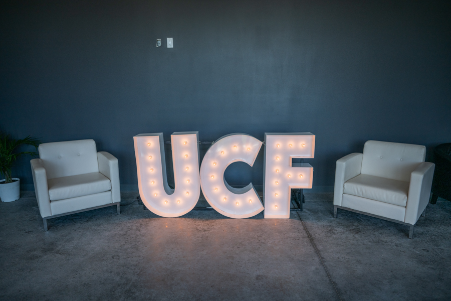 Illuminated UCF marquee letters between two white armchairs in a dim blue-walled room.