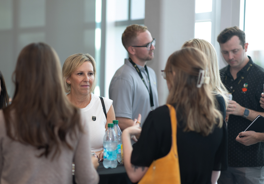 Group of professionals chatting around a high-top table in a bright office, with water bottles nearby, at a networking event.