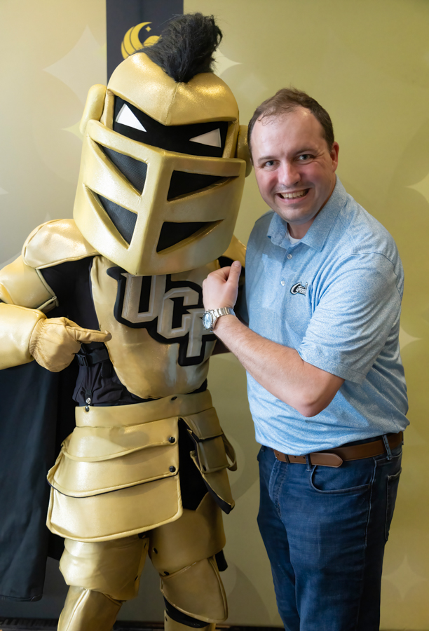Man posing with a large gold knight mascot in shiny armor, both smiling at the camera.