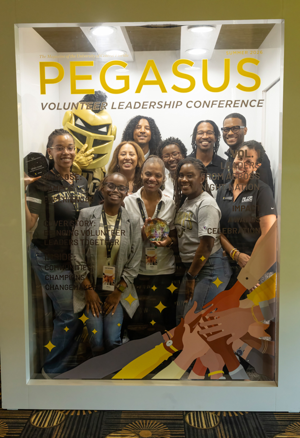 Diverse group of volunteers posing for a Pegasus Volunteer Leadership Conference banner (Summer 2026), wearing lanyards.
