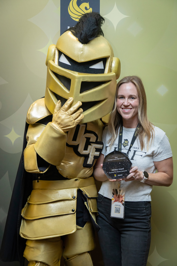 Woman poses with a gold knight mascot and an award at a UCF event.