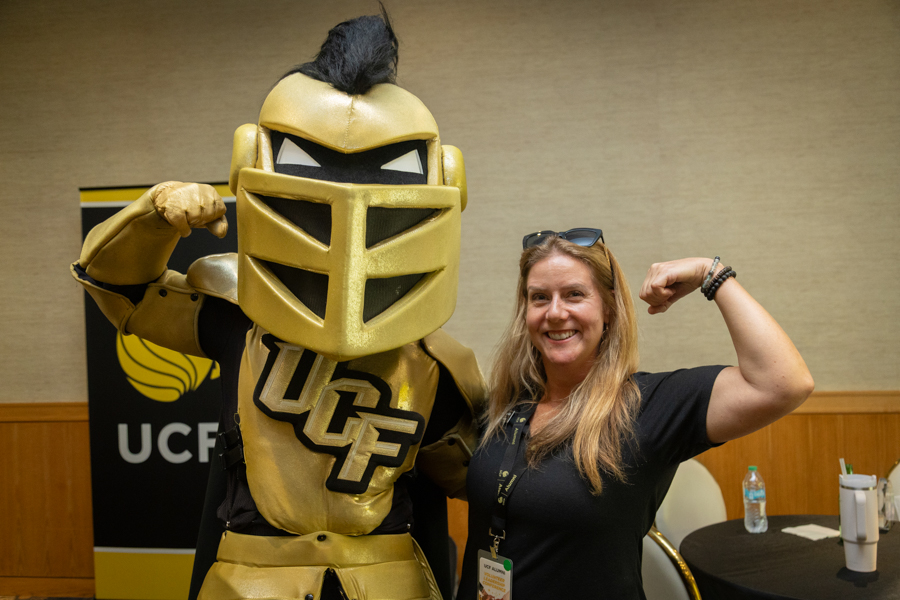 Woman posing with a gold knight mascot flexing its arm at a UCF event, smiling at the camera.