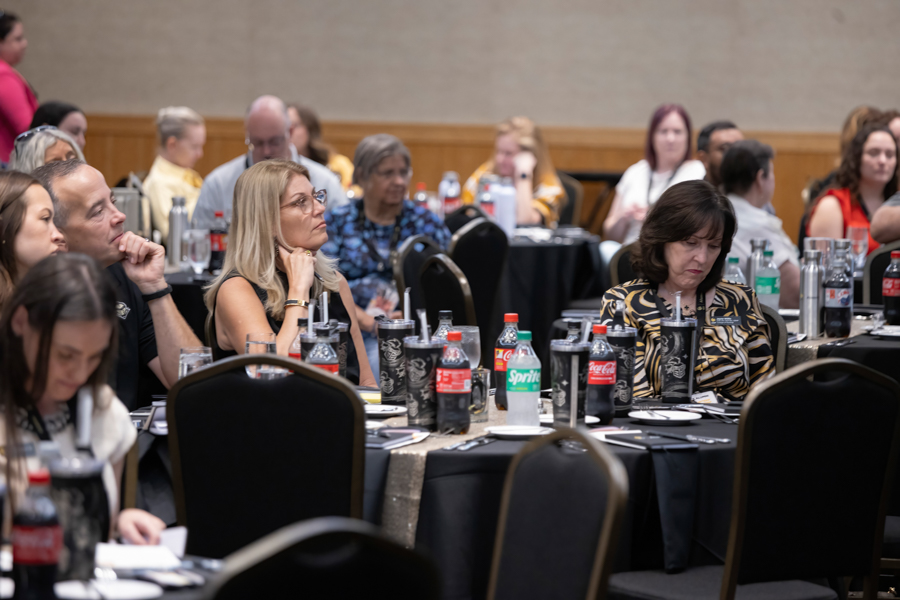 Audience seated at round banquet tables during a formal event, listening attentively to a speaker or presentation.