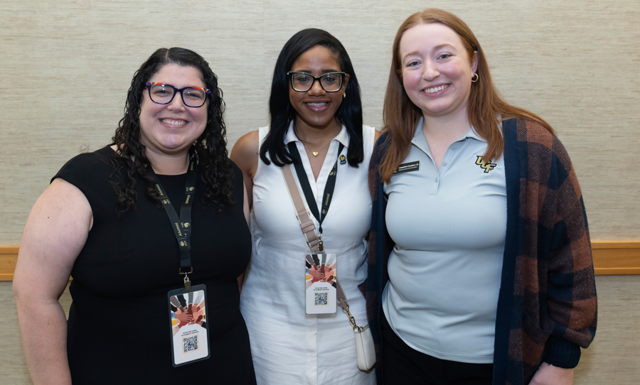 Three smiling women posing together at an event, each wearing a name badge on a lanyard.
