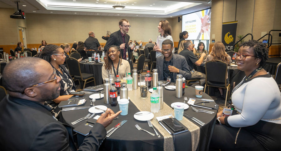 Group of professionals seated around a round table at a formal event, chatting and networking in a ballroom setting.