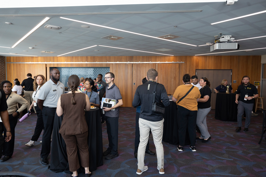 Professionals mingle around high-top tables at a conference networking event in a modern room.