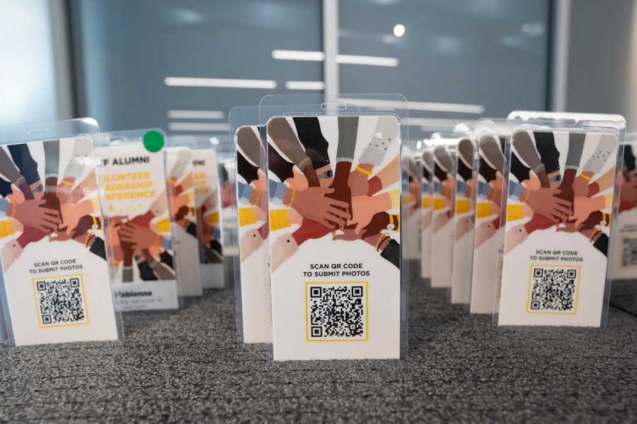 Pamphlets on a table showing many hands joining together, promoting teamwork and a QR code to submit photos.