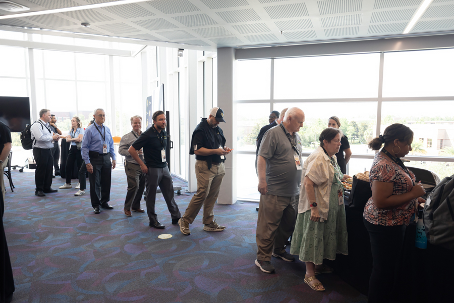 Attendees stand in a line at a registration area in a bright conference lobby as they wait to check in.