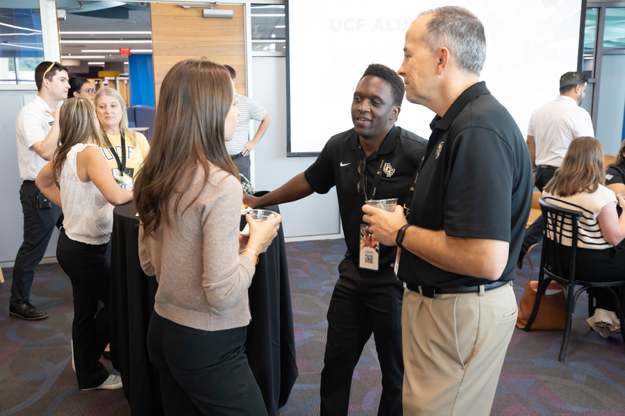 Group of professionals conversing around a tall cocktail table at a campus networking event.