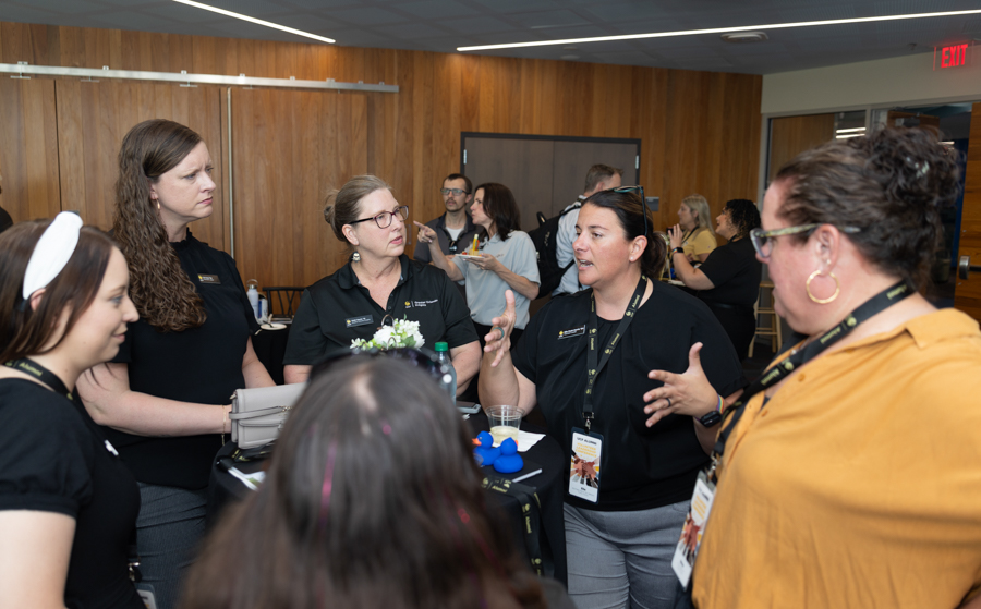Group of professionals at a round-table discussion during a conference, woman in black shirt speaking with hand gestures.