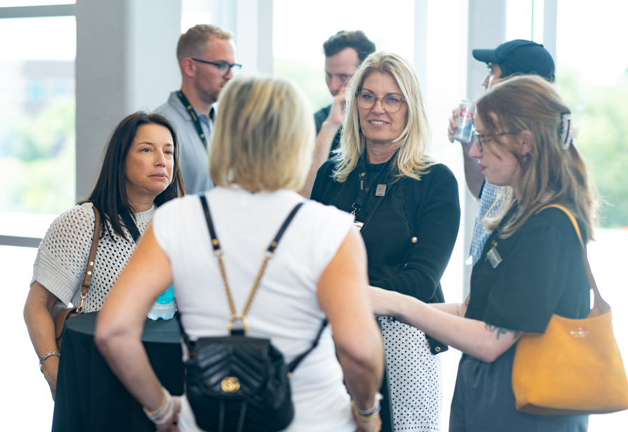 Group of professionals networking and chatting beside a bright windowed area at a conference.