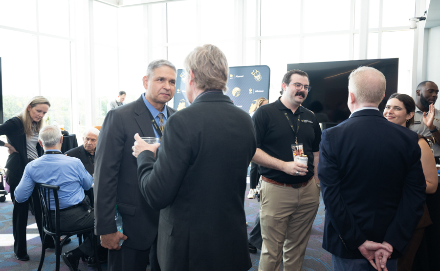 Group of professionals networking and chatting at a modern office event with large windows in the background.