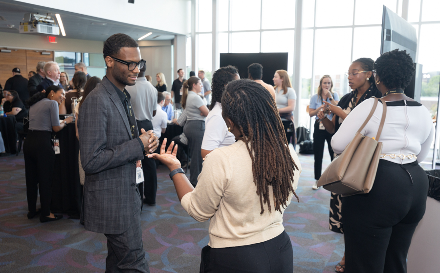 Professionals at a networking event chatting in a bright, modern venue with groups talking in the background.