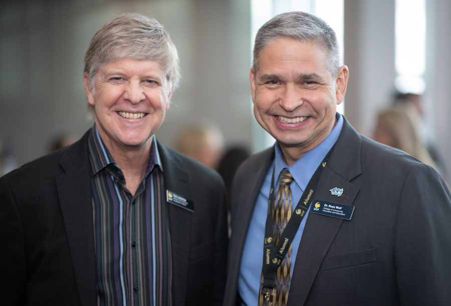 Two smiling men in suits at a networking event, wearing name badges and lanyards.