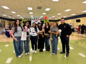 Group of young adults posing for a photo in a brightly lit event hall with balloons and tables in the background.