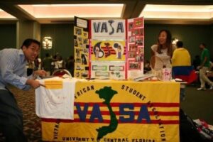 Vietnamese American Student Association booth with a yellow banner reading VASA and a map of Vietnam; two volunteers in a conference room.