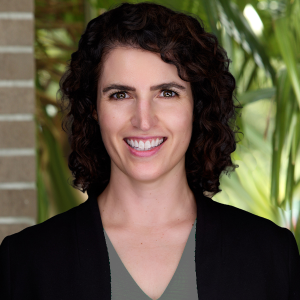 Smiling woman with dark curly hair in a black blazer outdoors, portrait-style headshot