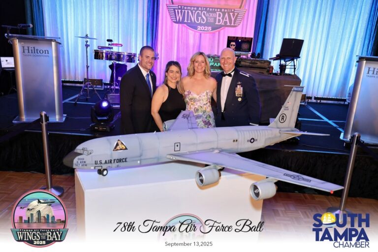 Four people in formal attire pose with a large model U.S. Air Force jet on display at Wings Across the Bay event, Tampa 2025 set on stage behind them.
