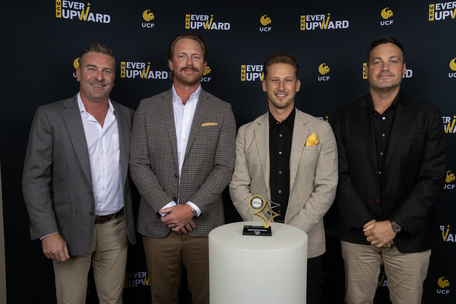 Four men in suits pose behind a white pedestal with a star-shaped trophy at an Ever Upward event backdrop.