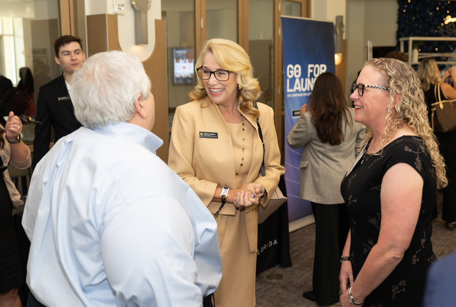 Three adults converse at a professional networking event in a lobby; a blue 'Go For Launch' banner is visible in the background.