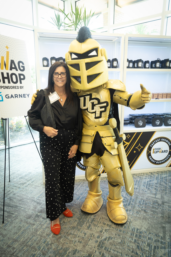 Woman posing with a gold knight mascot at a promo booth, giving a thumbs-up gesture.