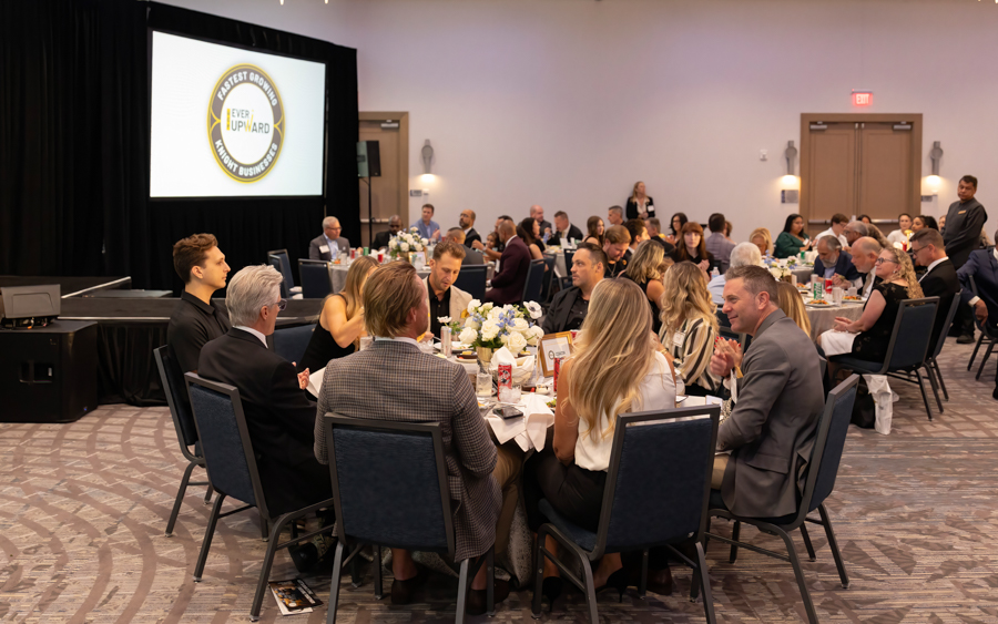 Professionals seated at round banquet tables during an awards gala, with a stage and presentation screen in the background.
