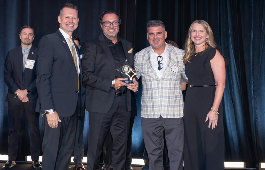 Group of five people on a stage at an awards ceremony; the man in the center holds a star-shaped trophy while the others smile.